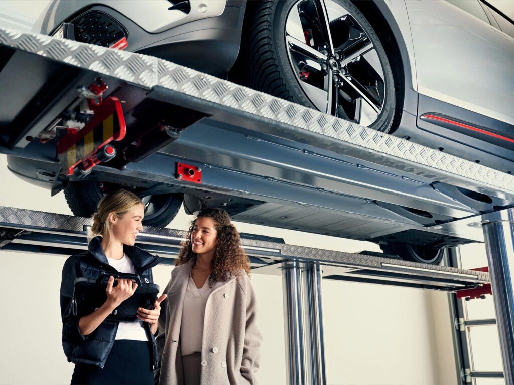 smart dealership service advisor talking to a smart electric car owner about warranty with the smart electric car on a hoist in the workshop 