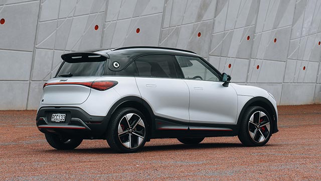 Rear side view of a white smart #1 electric car parked on red pebble outside a concrete building