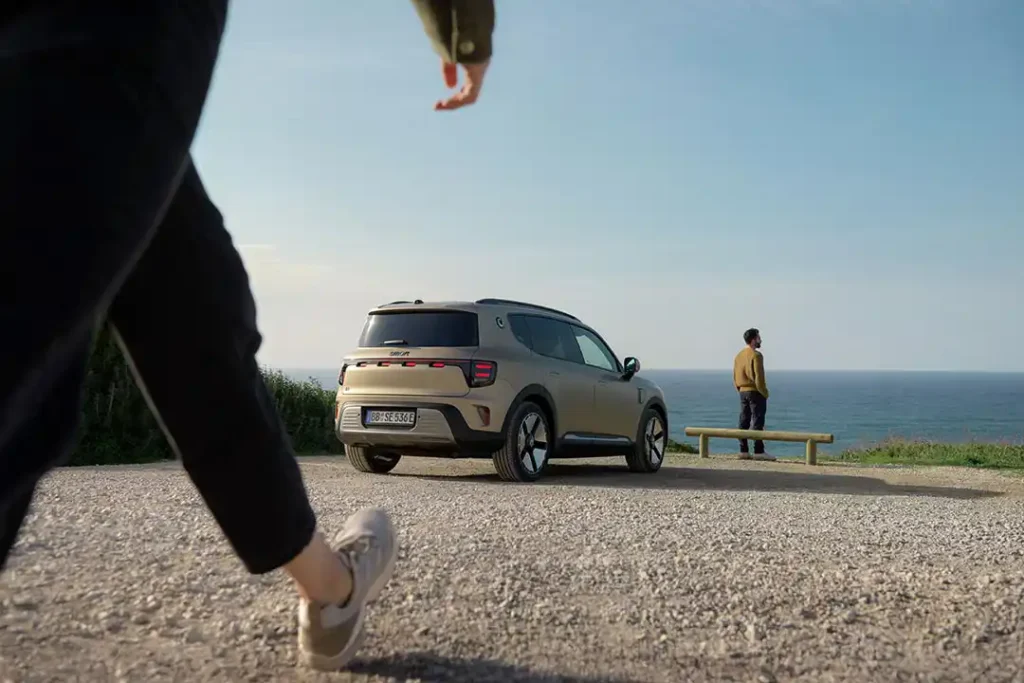 Rear three quarter view of a smart #5 electric SUV parked at a lookout next to the ocean with a man standing nearby looking out at the view.