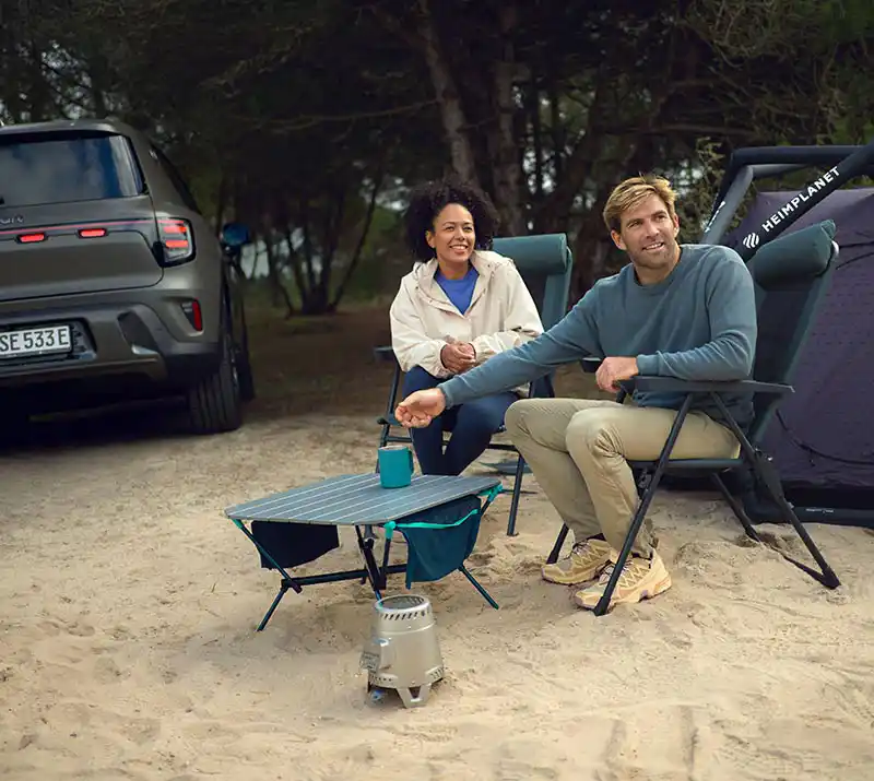 Man and woman sitting on camp chairs at their camping ground next to their tent and smart #5 electric SUV